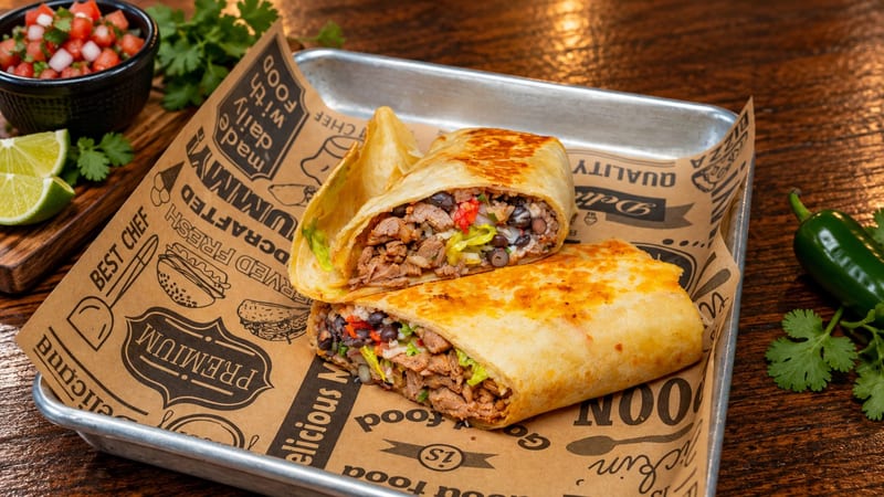 A grilled burrito cut in half, filled with steak, beans and peppers